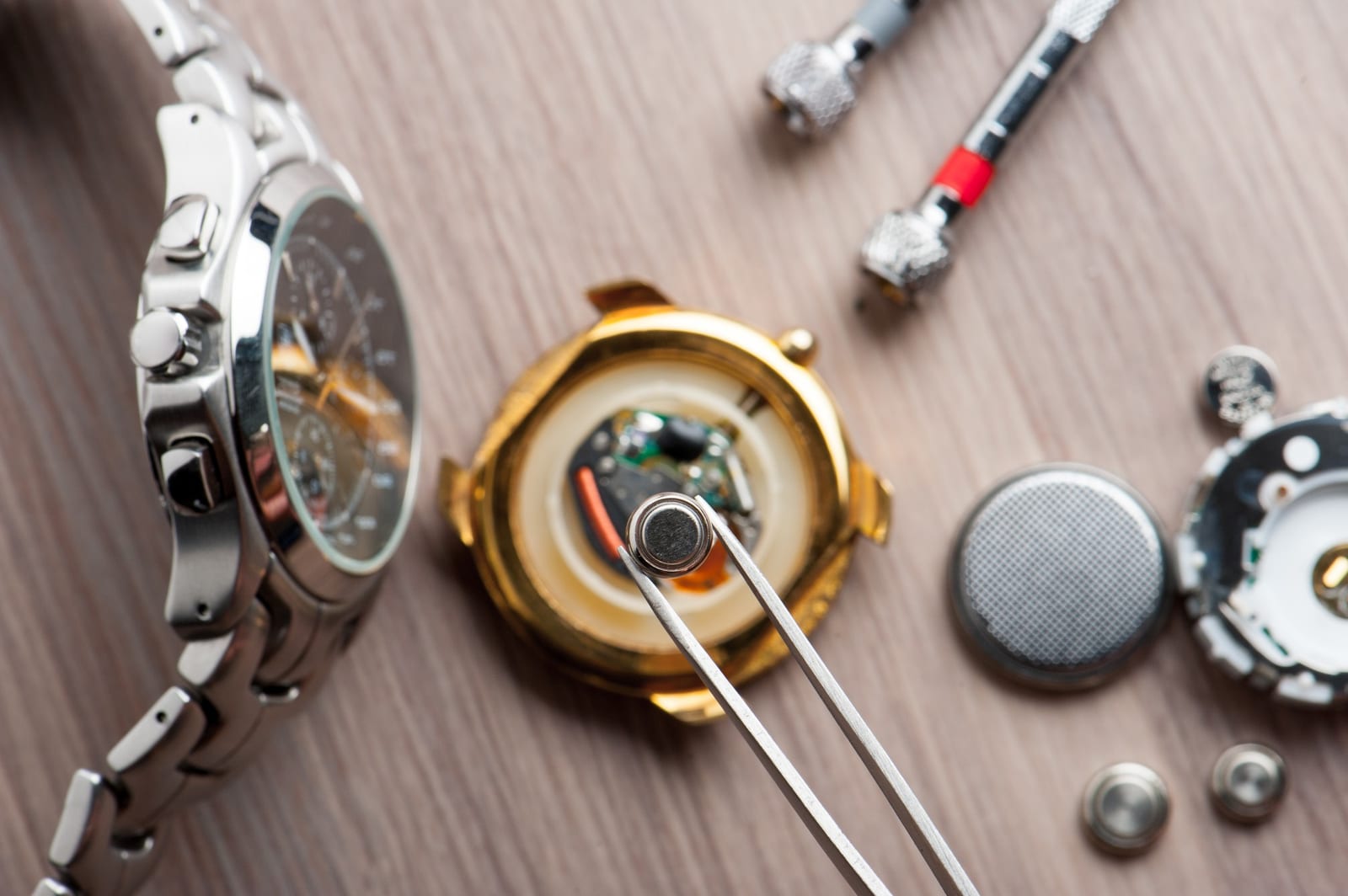 Pinzette da orologiaio su un fondello aperto, con cacciaviti e componenti sul banco